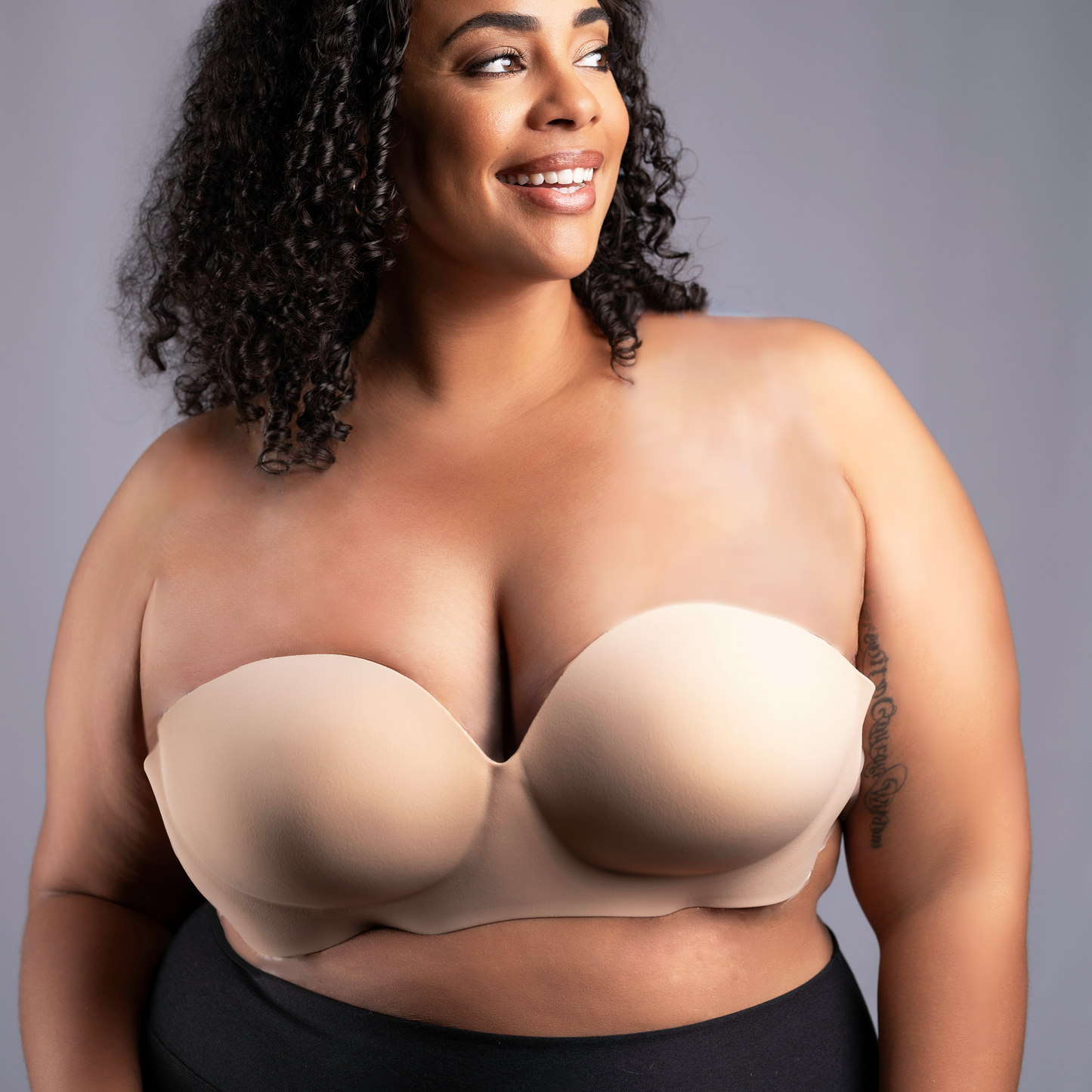 Model stands wearing the Voluptuous Backless Strapless Bra. It lifts and shapes without straps. Bra is nude in color.