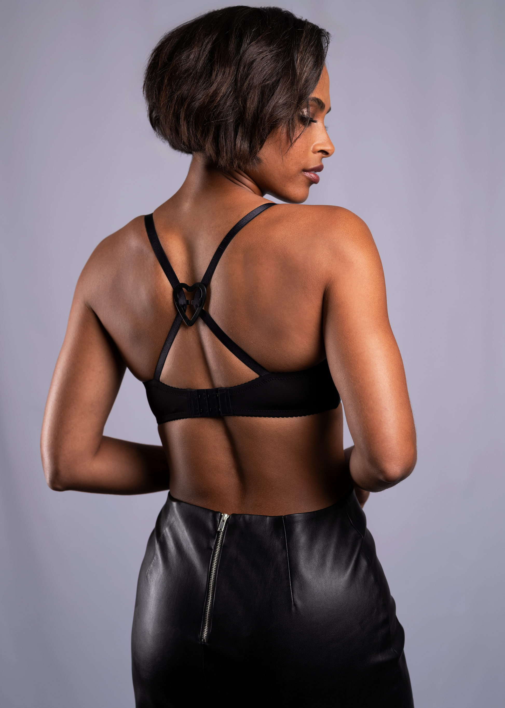 Strap solutions heart clip is holding bra straps together on the back of model, showing how it can turn the bra into a racerback. The clip is in the color black.