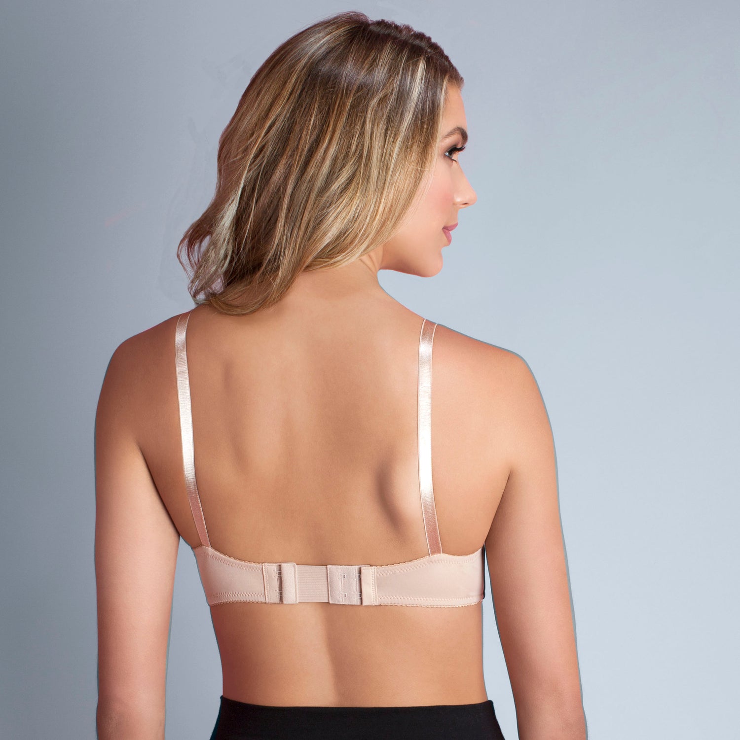 Model stands, back facing to the viewer wearing a bra using the nude 2 hook bra extender in beige, showing how it increases bra band size