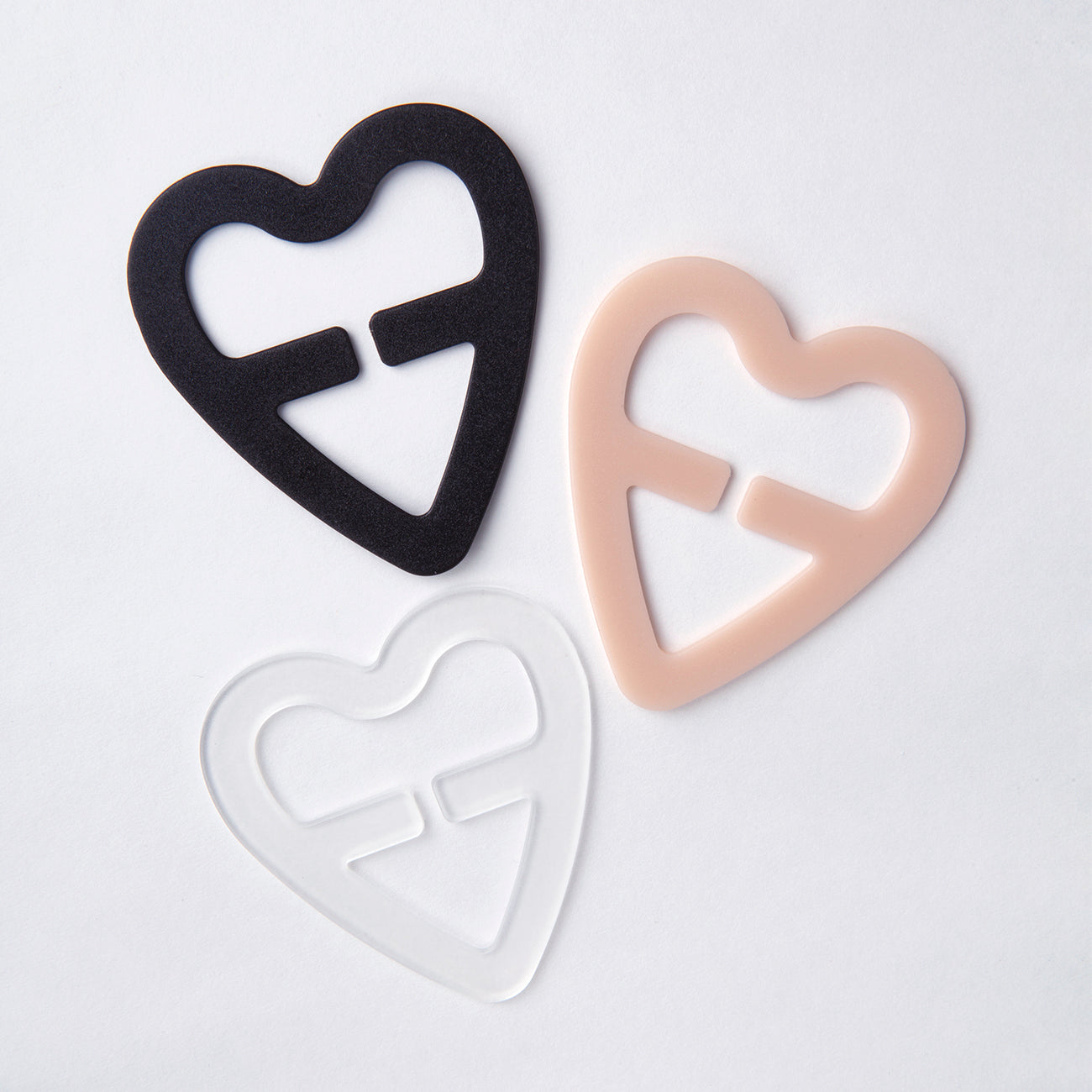 Close up product image of the heart shaped strap solutions clips in three colors: Black, white, and nude.